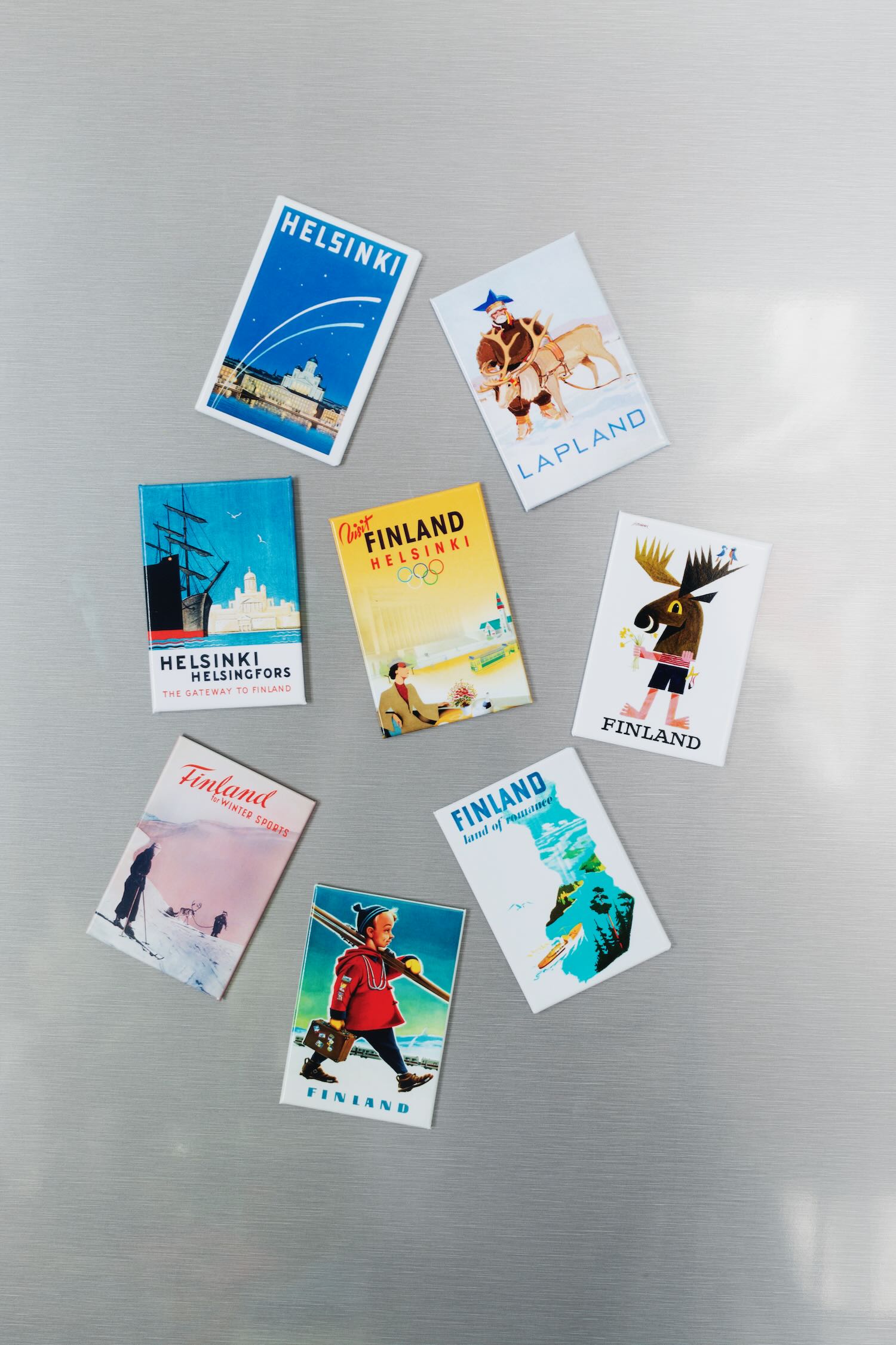 Sisustuskuva suomalaisesta matkajulisteesta painettu postikorttina, nimeltään “Suksipoika” painettuna jääkaappimagneetille.